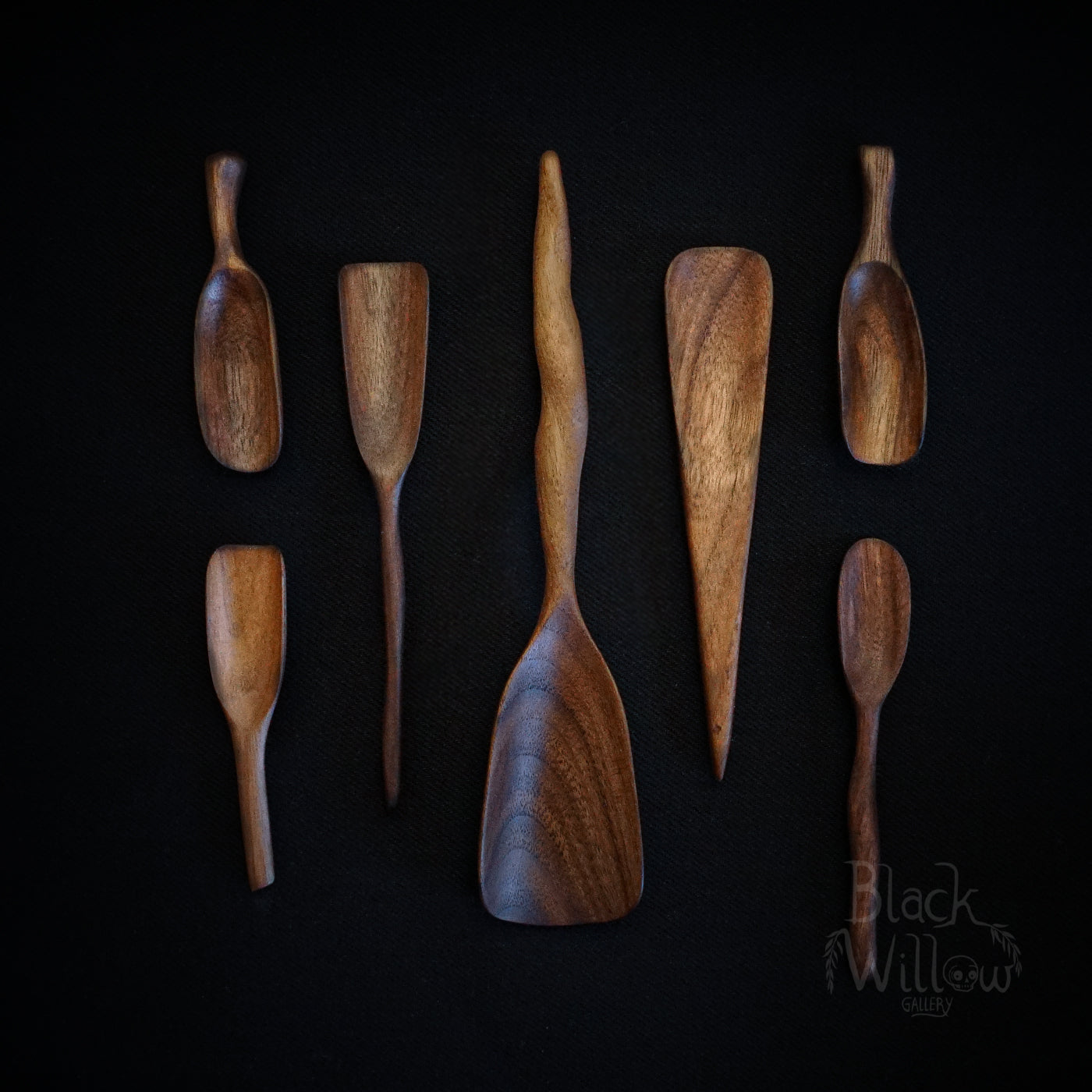 Seven handcrafted wooden scoops, arranged symmetrically on a solid black background. A 'Black Willow Gallery' brand watermark is visible in the bottom right corne
