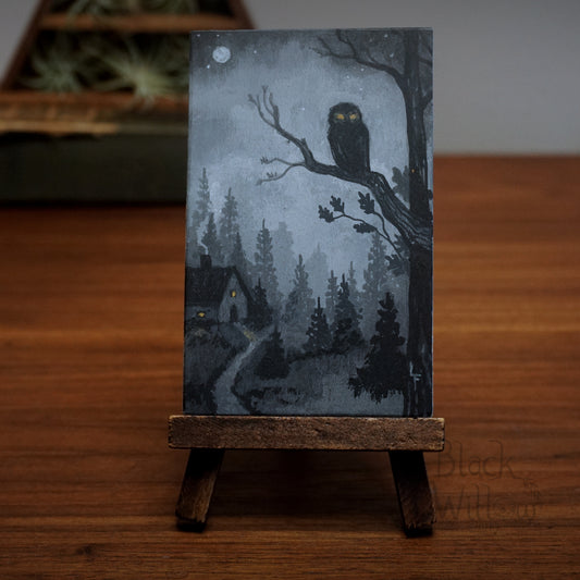 Artistic depiction of an owl on a branch with a house and trees in the background, displayed on a wooden stand.