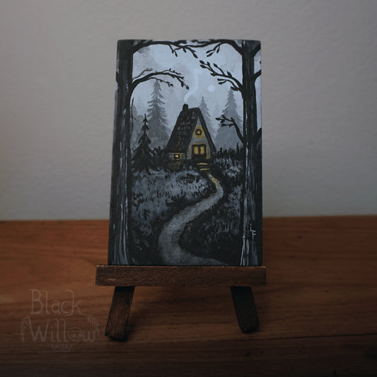 Artistic depiction of a house in the woods with a glowing light, on a stand against a plain background.