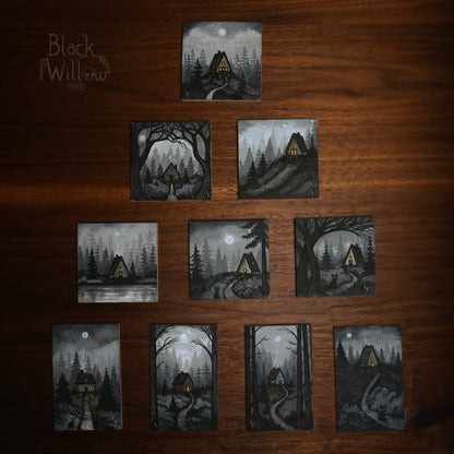 Set of 10 small paintings of a cabin in the woods on a wooden surface, with 'Black Willow Gallery' logo.
