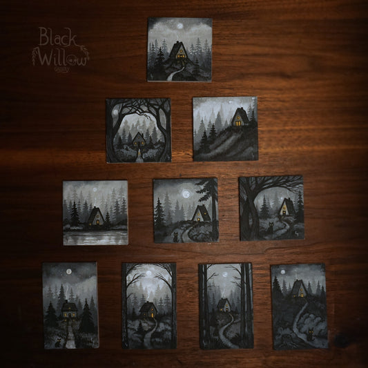 Set of 10 small paintings of a cabin in the woods on a wooden surface, with 'Black Willow Gallery' logo.