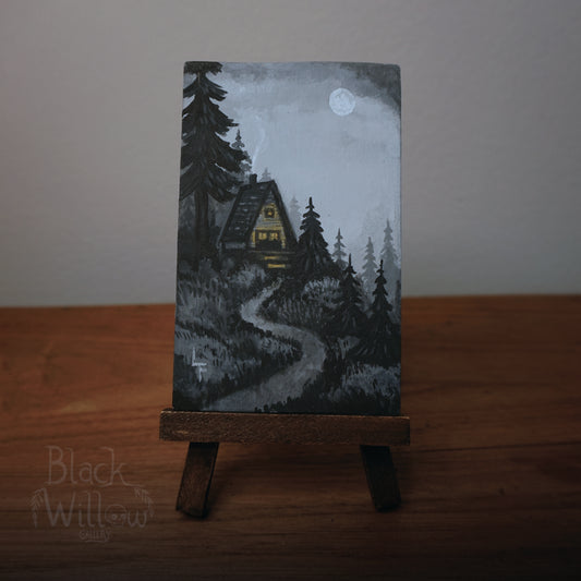 Miniature painting of a cabin in the woods on a stand with a dark background