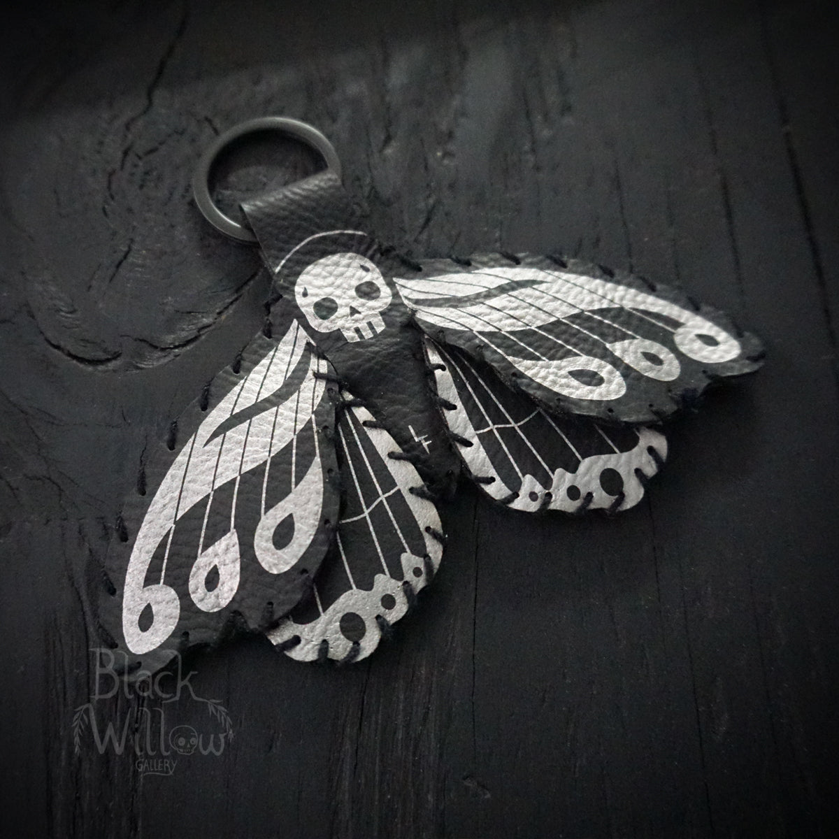 Death’s-head hawkmoth keychain made of black faux leather with silver details on dark background.
