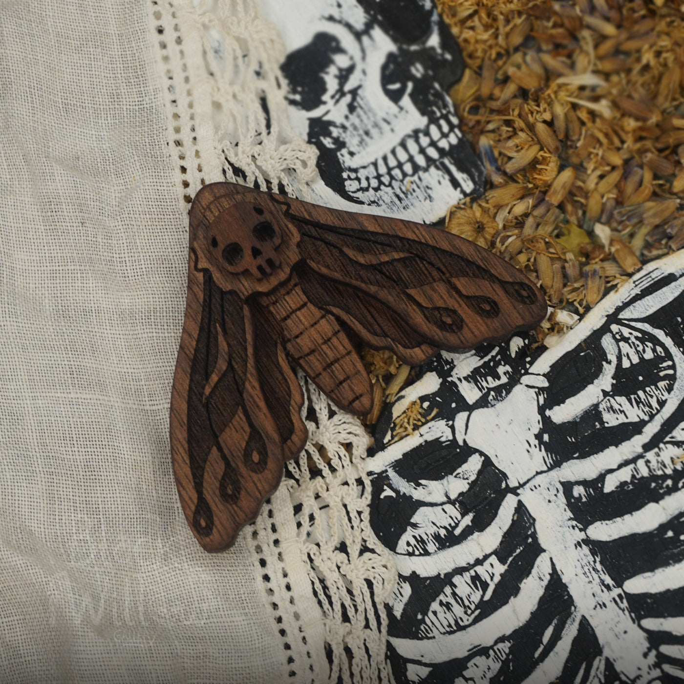 Wooden moth pin decorative item on a fabric background with skeleton and skull designs.